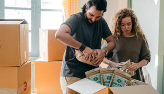 man and a woman packing kratom and other things inside a box near other boxes indoors