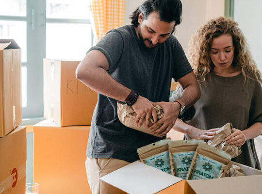 man and a woman packing kratom and other things inside a box near other boxes indoors